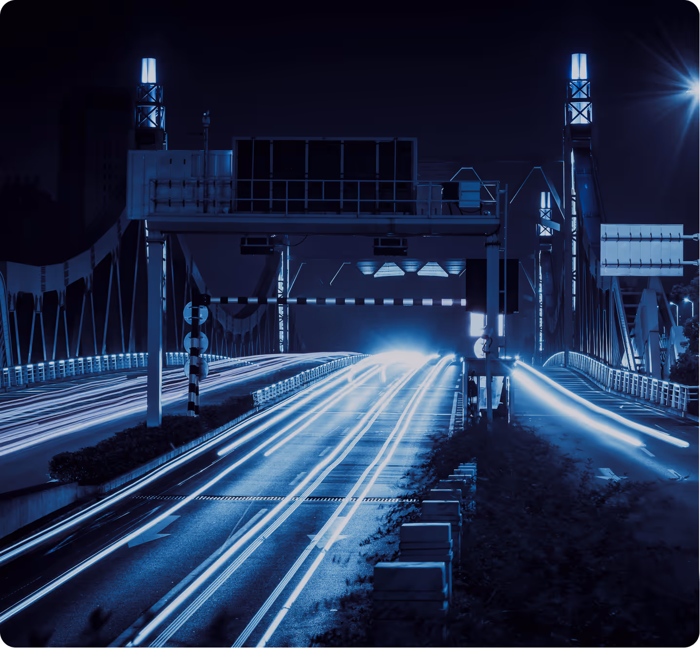 Nighttime long exposure of a bridge with bright blue light trails from moving vehicles.