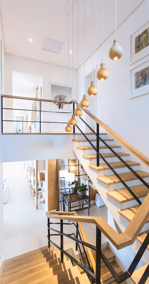 Escalier moderne intérieur en bois et métal avec des suspensions en forme d’ampoules en bois, décor minimaliste et lumineux dans une maison contemporaine à étage.