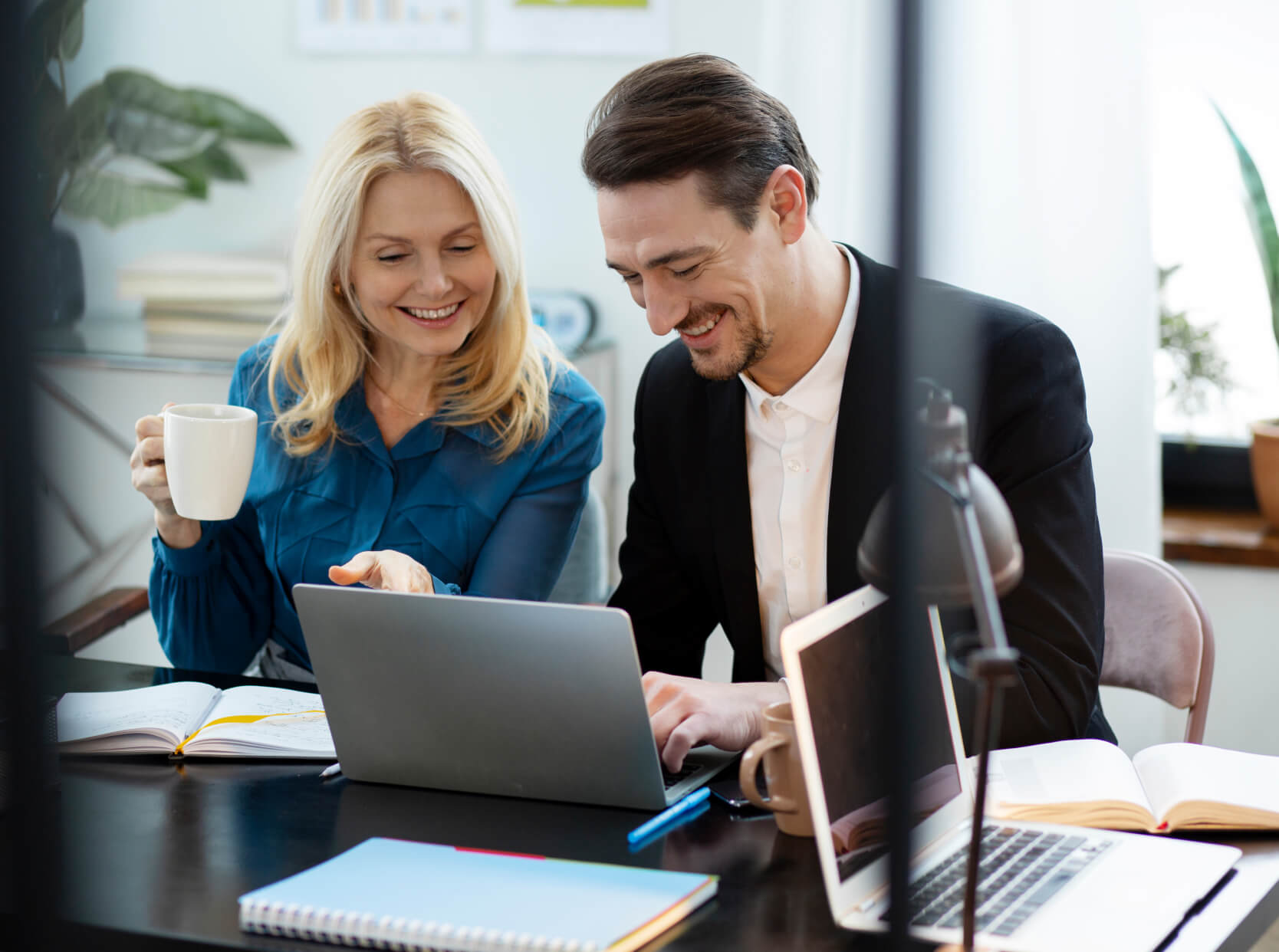 A man and a woman sitting at a desk looking at a laptop.