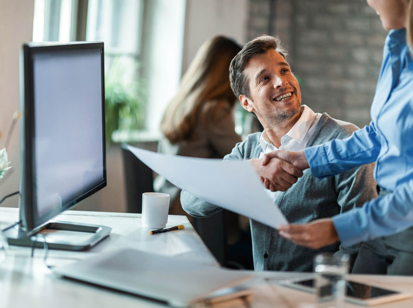 Two people shaking hands in front of a computer screen.