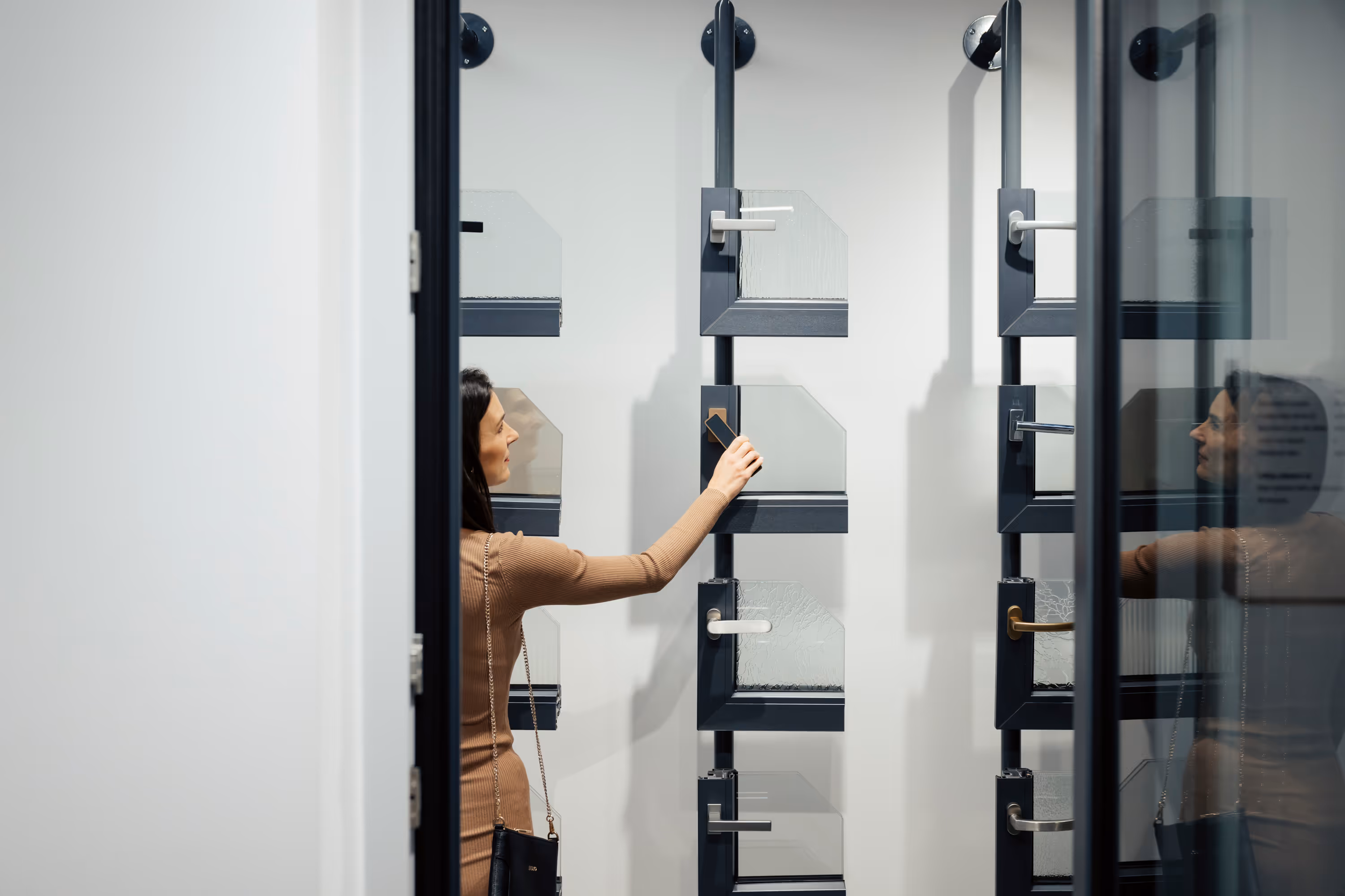 Žena kontroluje a vybírá vzorky skleněných dveří z vystaveného stojanu ve vzorkové prodejně.