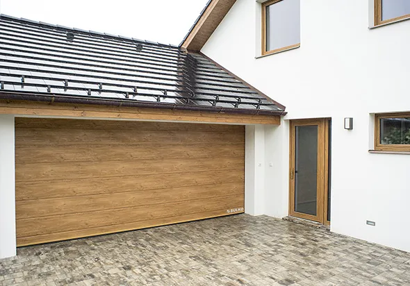 Moderní dům s velkou garážovou vratou s dřevěným vzhledem a vedlejším dveřím s dřevěným rámem.