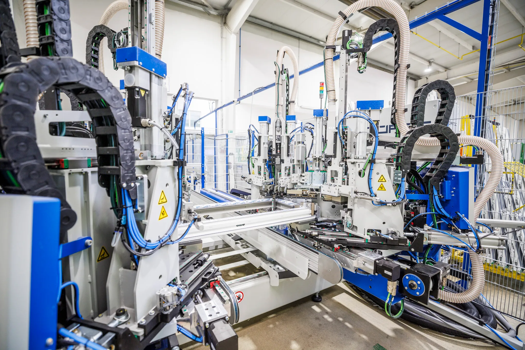 Automatizovaný výrobní stroj s modrými a bílými komponenty v průmyslové hale.