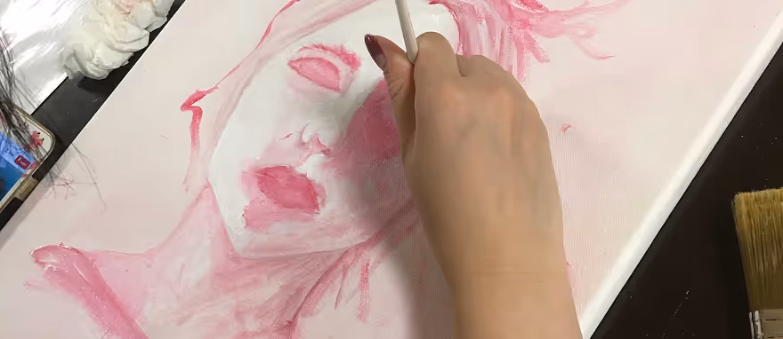 Hånd som maler en rosa kvinneportrett med en pensel på et lerret.