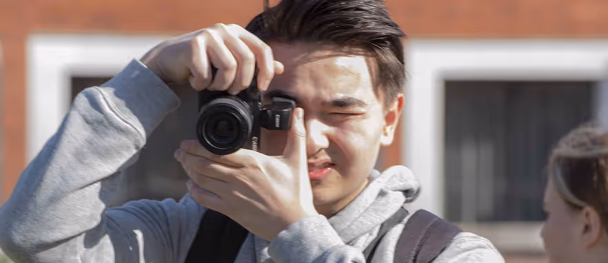 Ung mann i grå hettegenser som tar bilde med kamera utendørs.