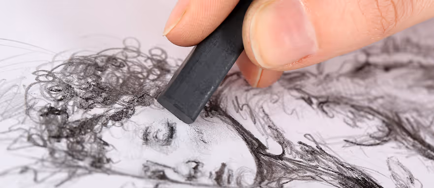 Hånd som bruker en svart kritt til å tegne et portrett med krøllete hår på papir.