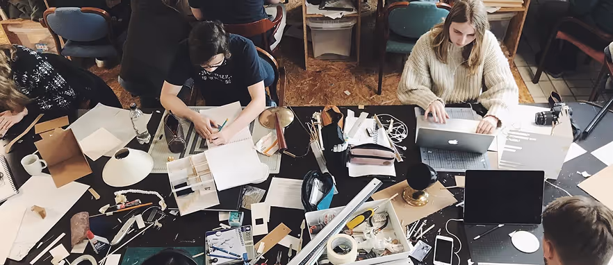 Flere personer jobber med papir, bærbare datamaskiner og forskjellige kontorrekvisita rundt et stort bord.