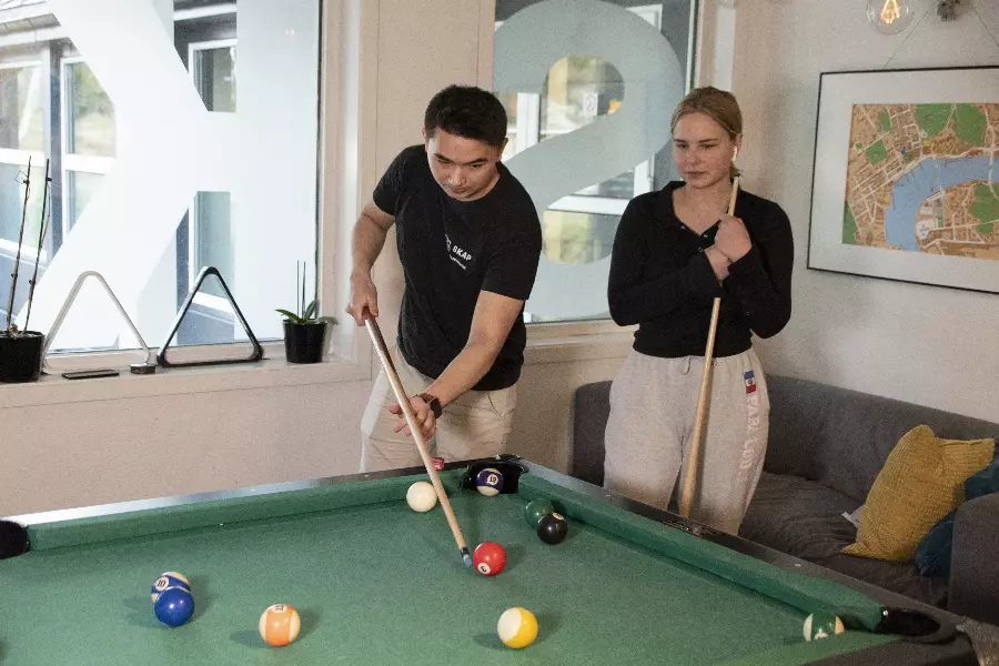 To personer spiller biljard i et rom med store vinduer og et veggkart.