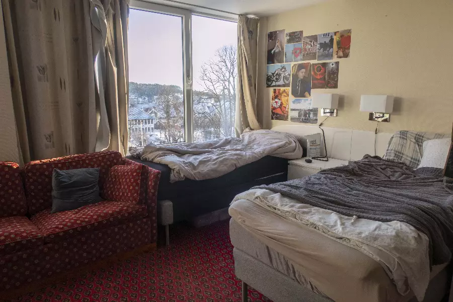 Soverom med to senger, et rødt mønstret teppe, en rød sofa med pute, gardiner og store vinduer som viser et snødekt landskap utenfor.