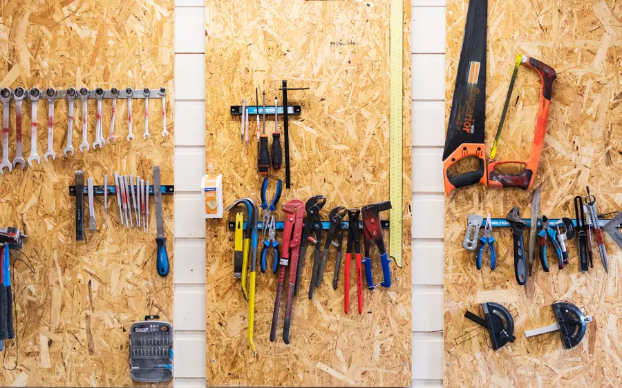 Verktøy som henger organisert på en trevegg, inkludert skiftenøkler, filer, tang, rørkuttere, håndsager og vater.