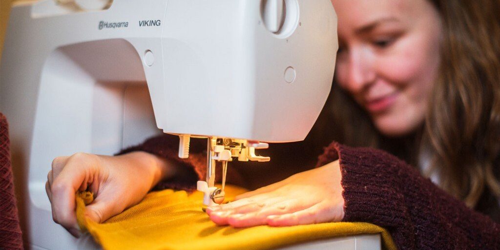 Person som syr en gul tekstil på en Husqvarna Viking symaskin, med fokus på hendene og maskinen.