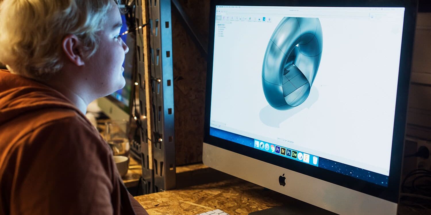 Person with blond hair looking at a 3D design of a curved shape on an Apple iMac computer screen.