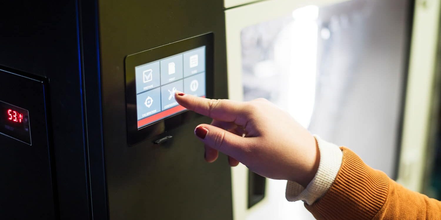 En person med oransje genser trykker på en berøringsskjerm på en maskin.