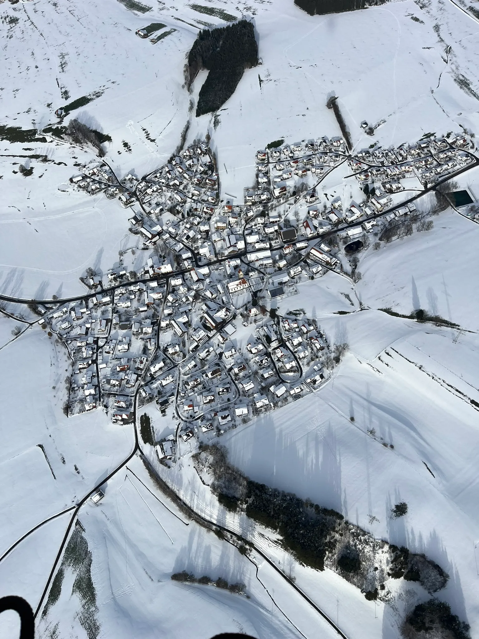 Luftaufnahme einer kleinen verschneiten Stadt mit verstreuten Häusern und verschneiten Feldern im Winter.