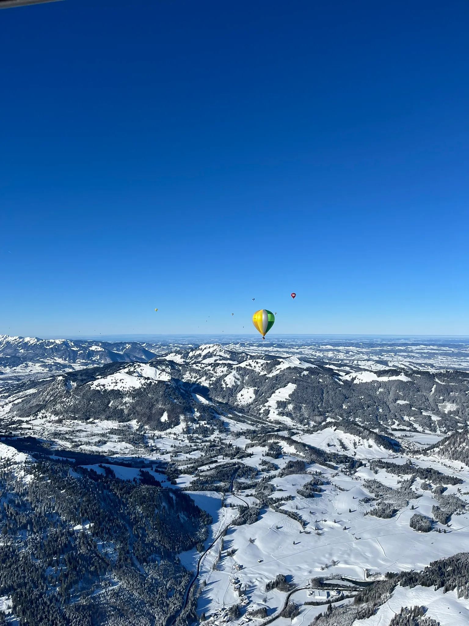 Heißluftballons fliegen über schneebedeckte Berge und Täler unter klarem blauem Himmel.