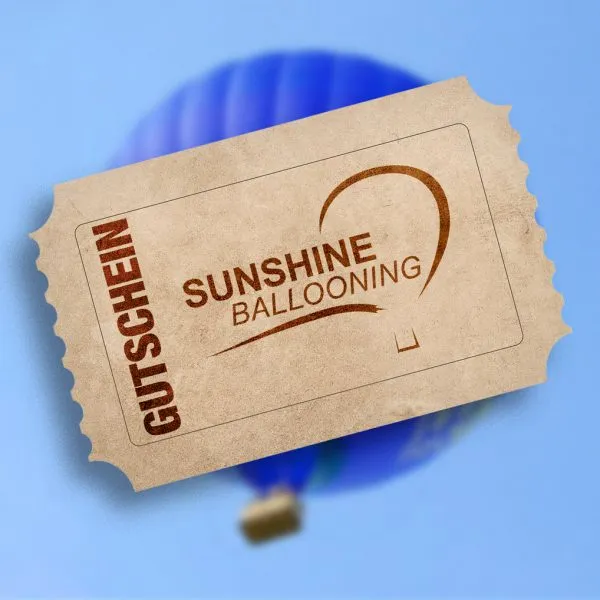 Geschenkgutschein von Sunshine Ballooning mit braunem Heißluftballon-Logo vor einem unscharfen blauen Heißluftballon-Hintergrund.