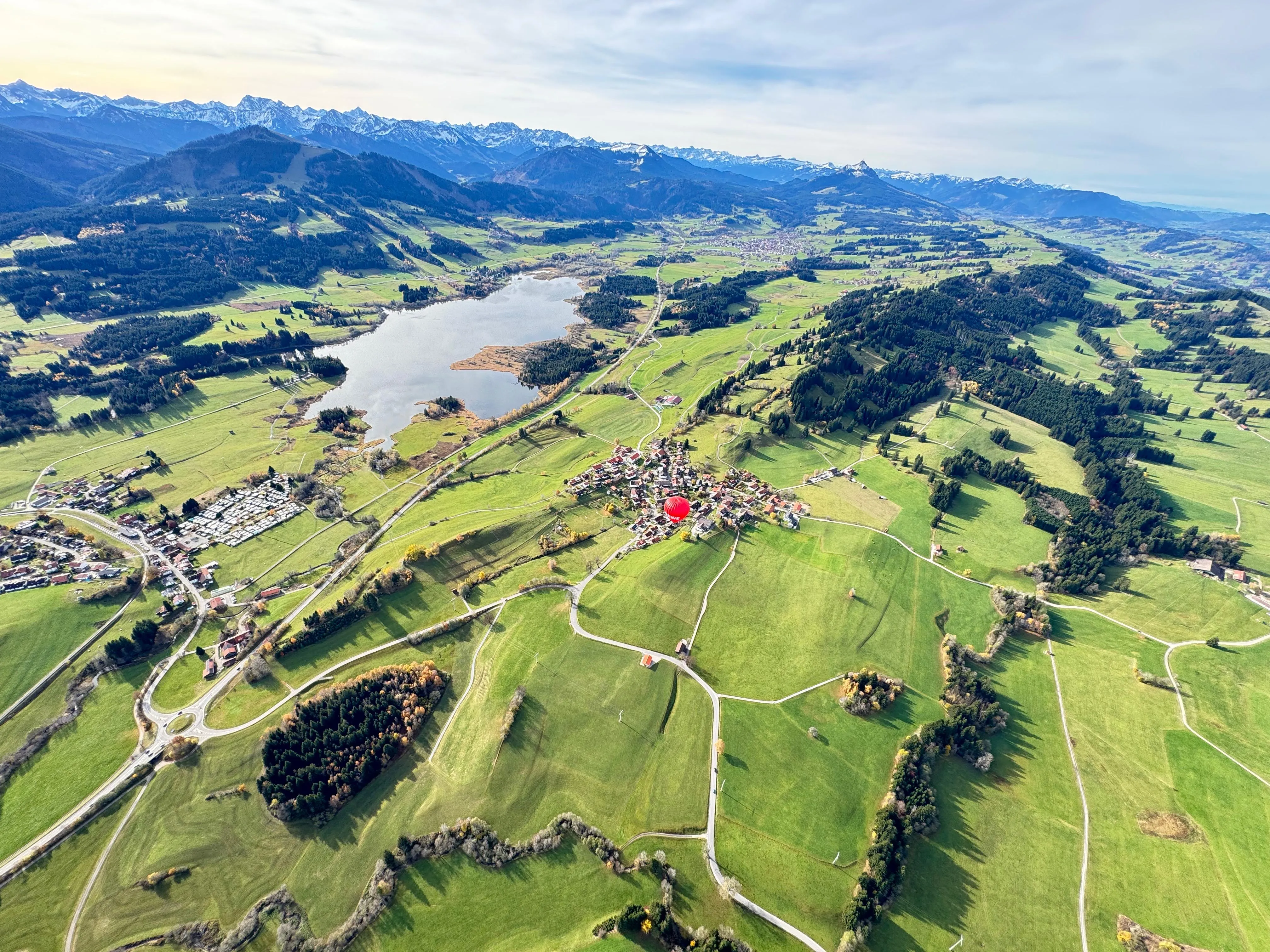 Eine Luftaufnahme einer grünen Landschaft mit einem See, verstreuten Dörfern und einem roten Heißluftballon in der Mitte.
