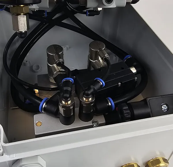 Nahaufnahme von Metallventilen und schwarzen Schläuchen mit blauen Dichtungen in einem grauen Gehäuse.