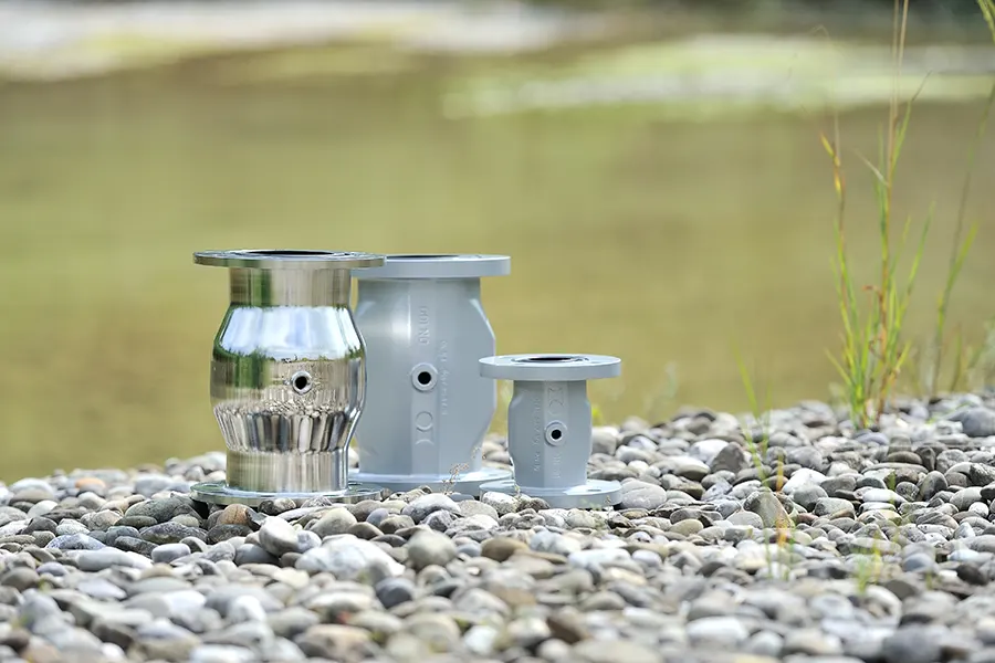 Drei unterschiedlich große Rohrventile auf Kies mit unscharfem Hintergrund aus Gras und Wasser.