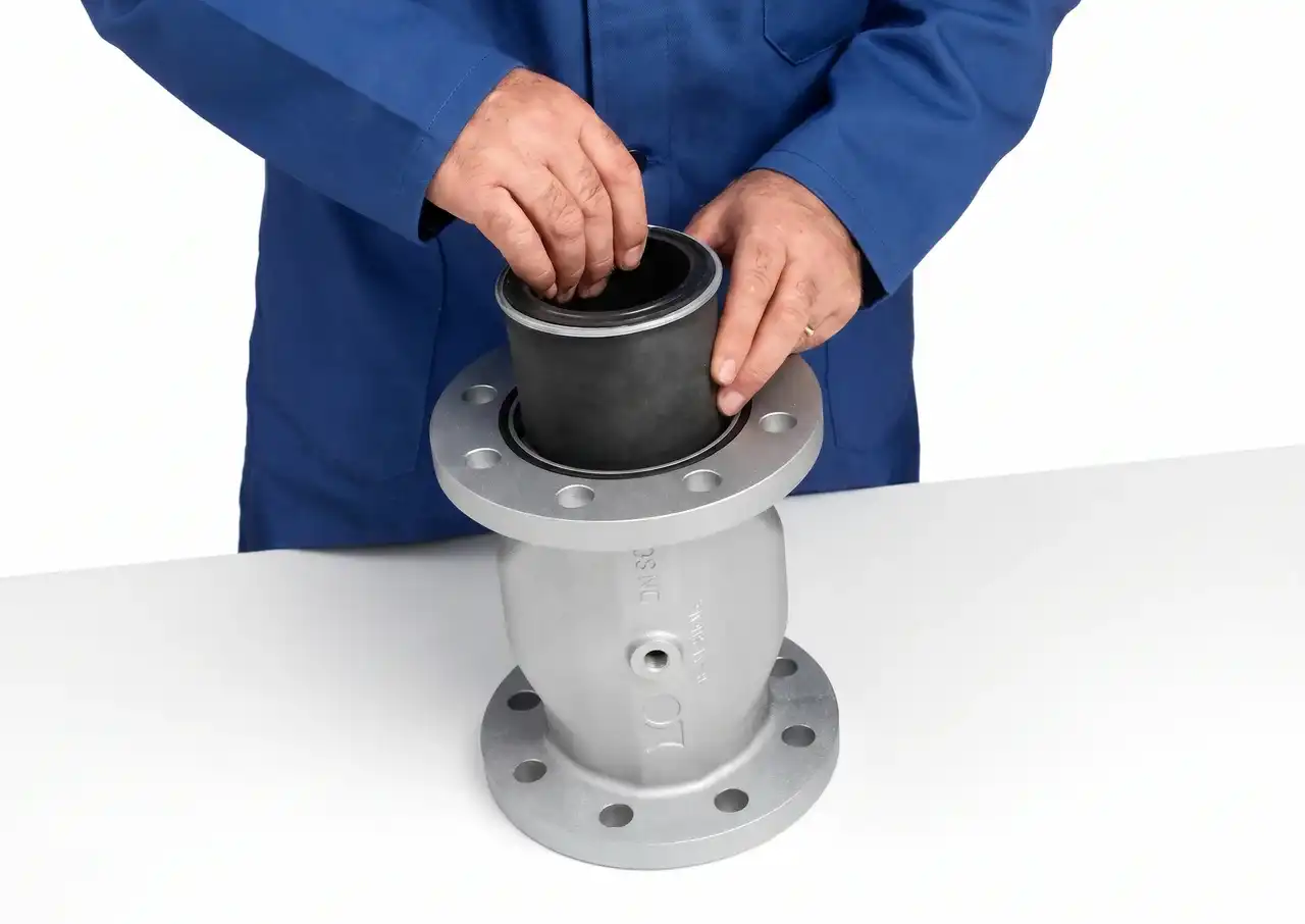 Person in blauer Arbeitskleidung setzt eine schwarze Manschette in ein Metallrohr mit Flanschen ein.