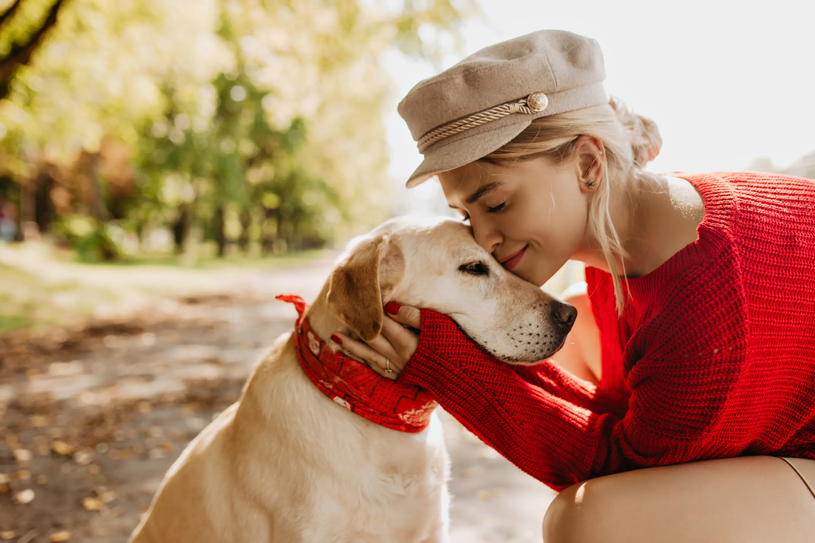 Un bisous a son bébé chien par une fille habillée en pull rouge et portant une casquette