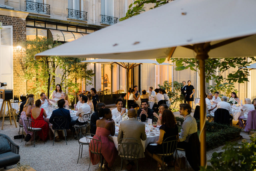 Guests enjoying an elegant outdoor dinner party at night under large umbrellas in a courtyard.