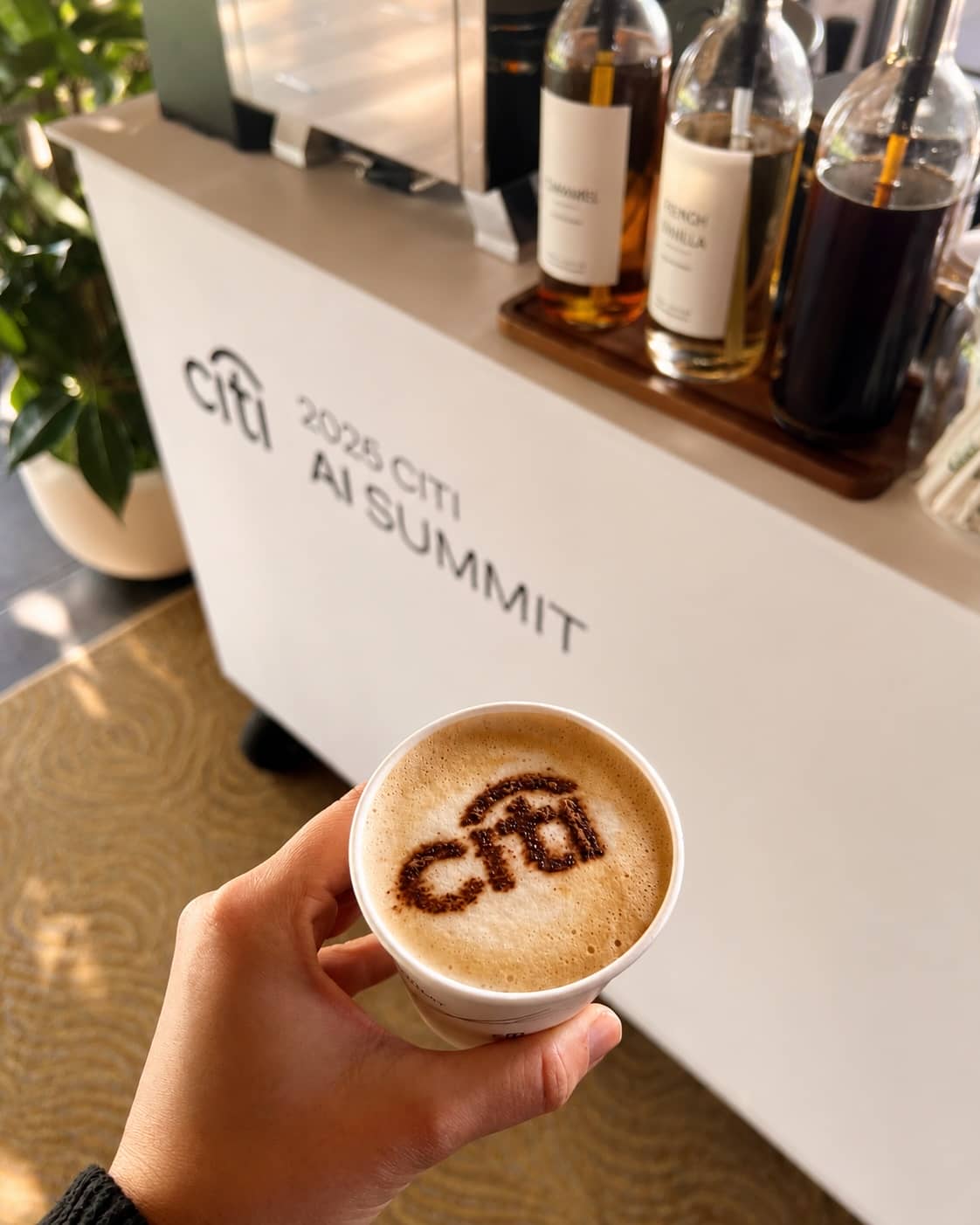Hand holding an Espresso Station latte with a Citi logo dusted on the foam at a corporate event