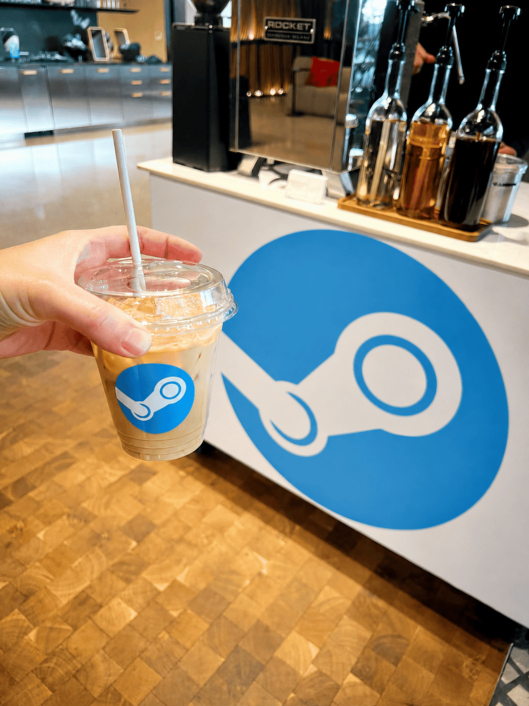 Hand holding an iced Espresso Station latte in a Steam-branded cup at a corporate event