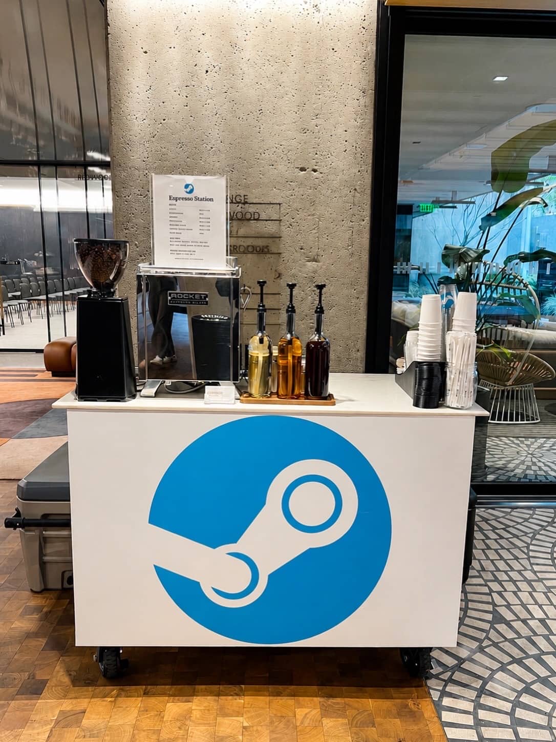 Espresso Station coffee cart with a Steam logo decal in a stone-walled corporate lobby