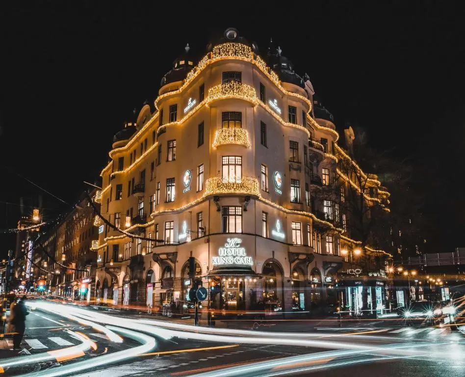 Vackert upplyst hotell i centrala Stockholm på kvällen med julbelysning och livlig trafik runt byggnaden.
