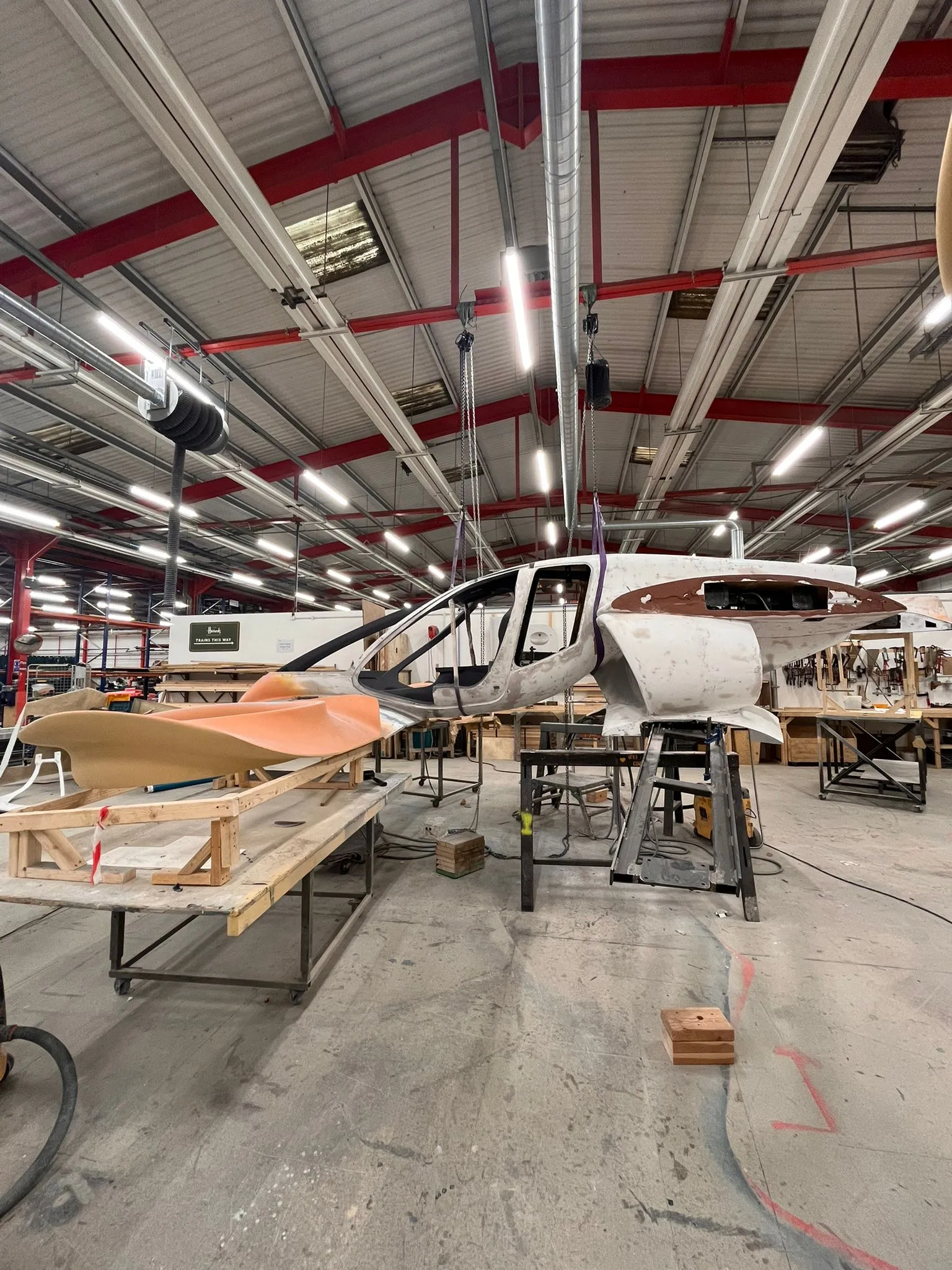 Side view of the partially assembled Doroni aircraft prototype suspended in a workshop, with its cockpit structure exposed and aerodynamic body panels in progress.