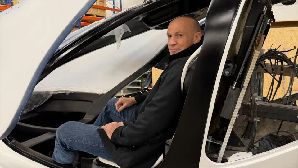 Front view of the suspended Doroni eVTOL prototype in a fabrication workshop, showcasing its aerodynamic curves, cockpit framework, and ducted fan housings under construction.