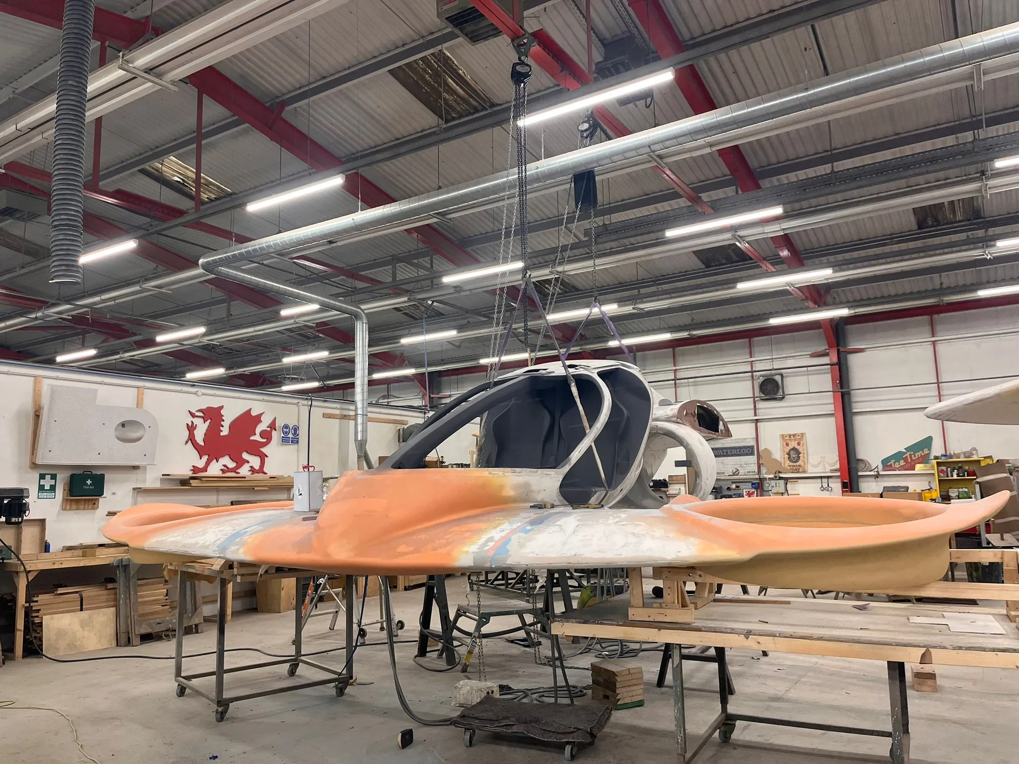 Front view of the suspended Doroni eVTOL prototype in a fabrication workshop, showcasing its aerodynamic curves, cockpit framework, and ducted fan housings under construction.