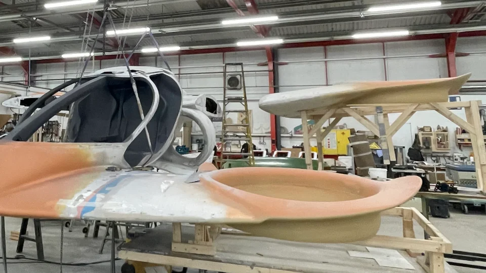 Early-stage assembly of Doroni’s aircraft prototype inside a workshop, with cockpit structure suspended from a ceiling hoist and wings under construction nearby.