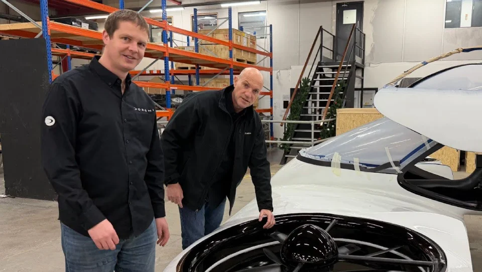 Front view of the suspended Doroni eVTOL prototype in a fabrication workshop, showcasing its aerodynamic curves, cockpit framework, and ducted fan housings under construction.