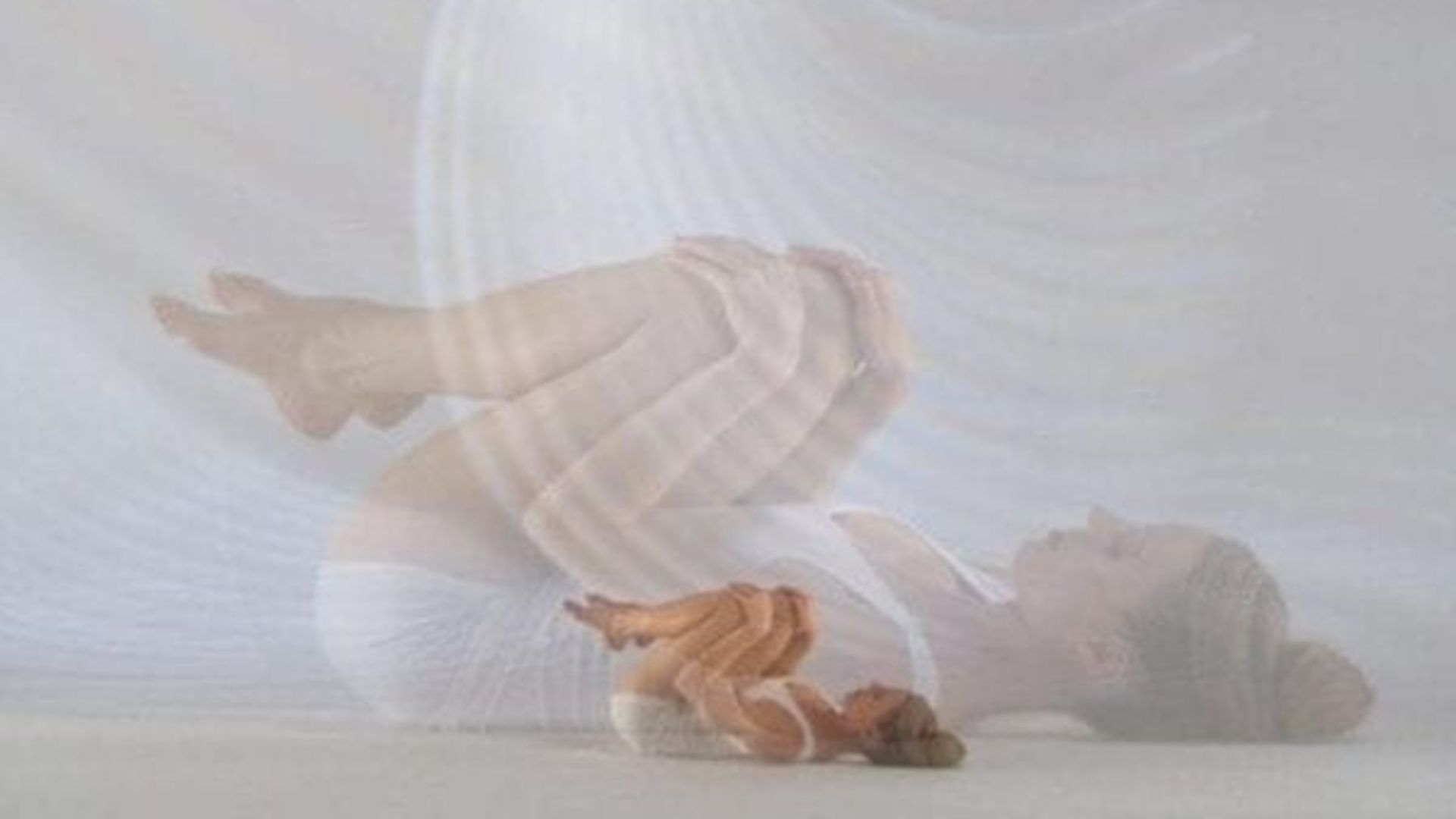 A woman sits on the floor with her legs raised, appearing relaxed and contemplative in her surroundings.