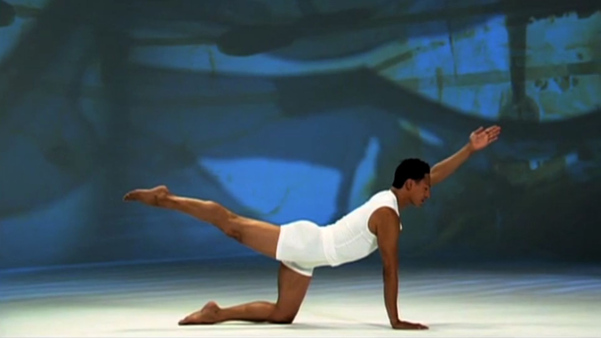 A person wearing white athletic attire performs a yoga pose on a neutral stage. The background has soft, abstract colors, creating a calm ambiance.