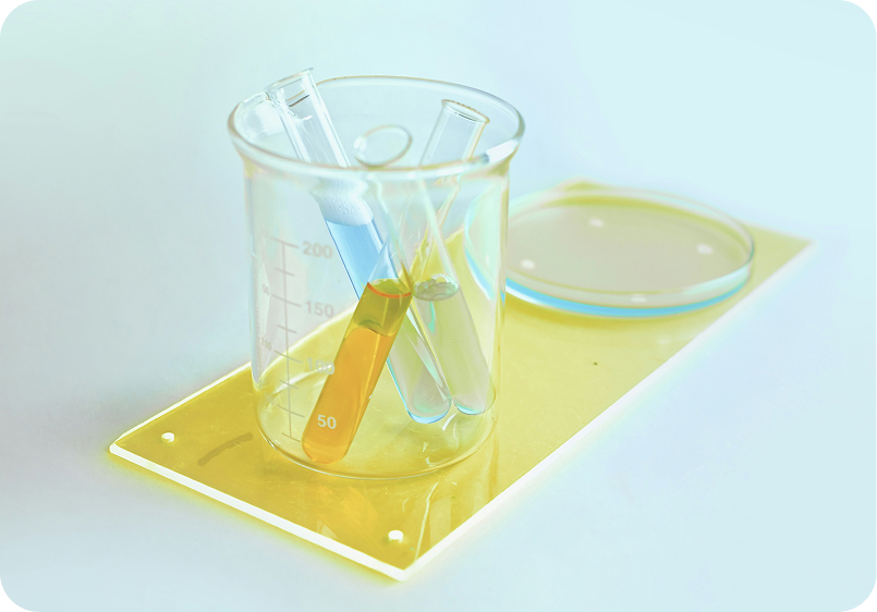 Three test tubes with colored liquids inside a clear glass beaker, placed on a yellow tray alongside a petri dish.