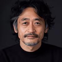 Portrait of a middle-aged man with black hair and a short beard wearing a black sweater against a dark background.