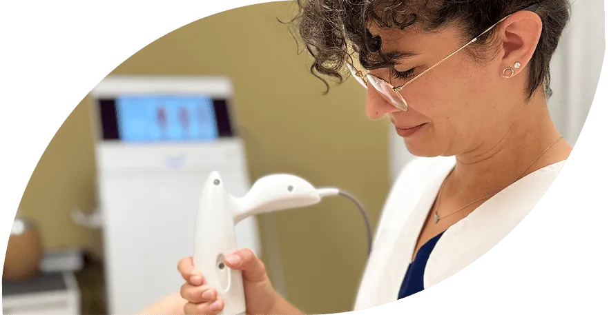 Medical professional with glasses holding a white handheld device in a clinical setting.