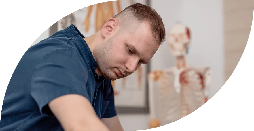Focused man with a short haircut wearing a navy blue shirt in a medical or anatomical study setting with a human skeleton model in the background.