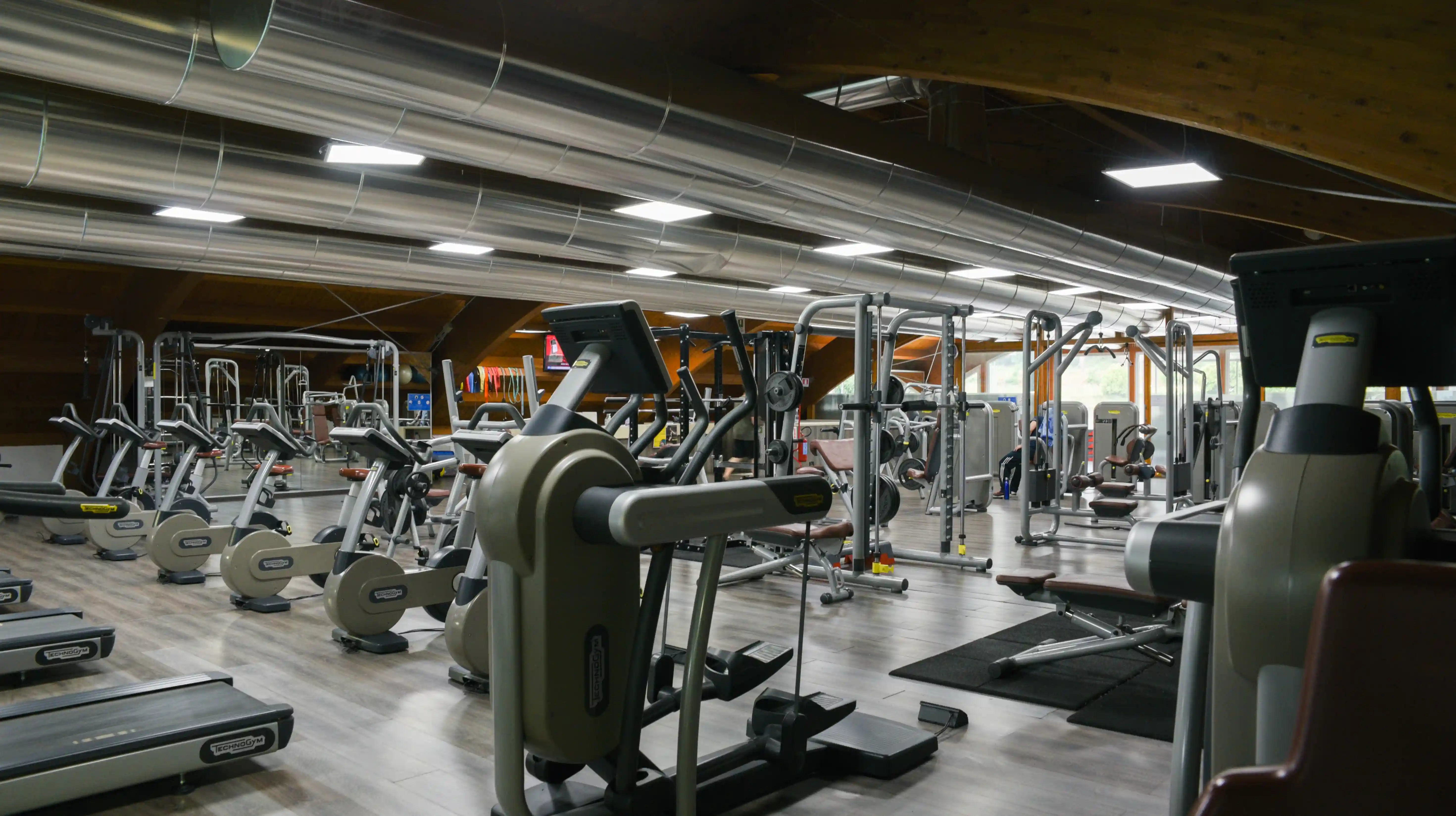 Interno di una palestra moderna con attrezzature per il fitness come cyclette, tapis roulant e macchine per il sollevamento pesi.