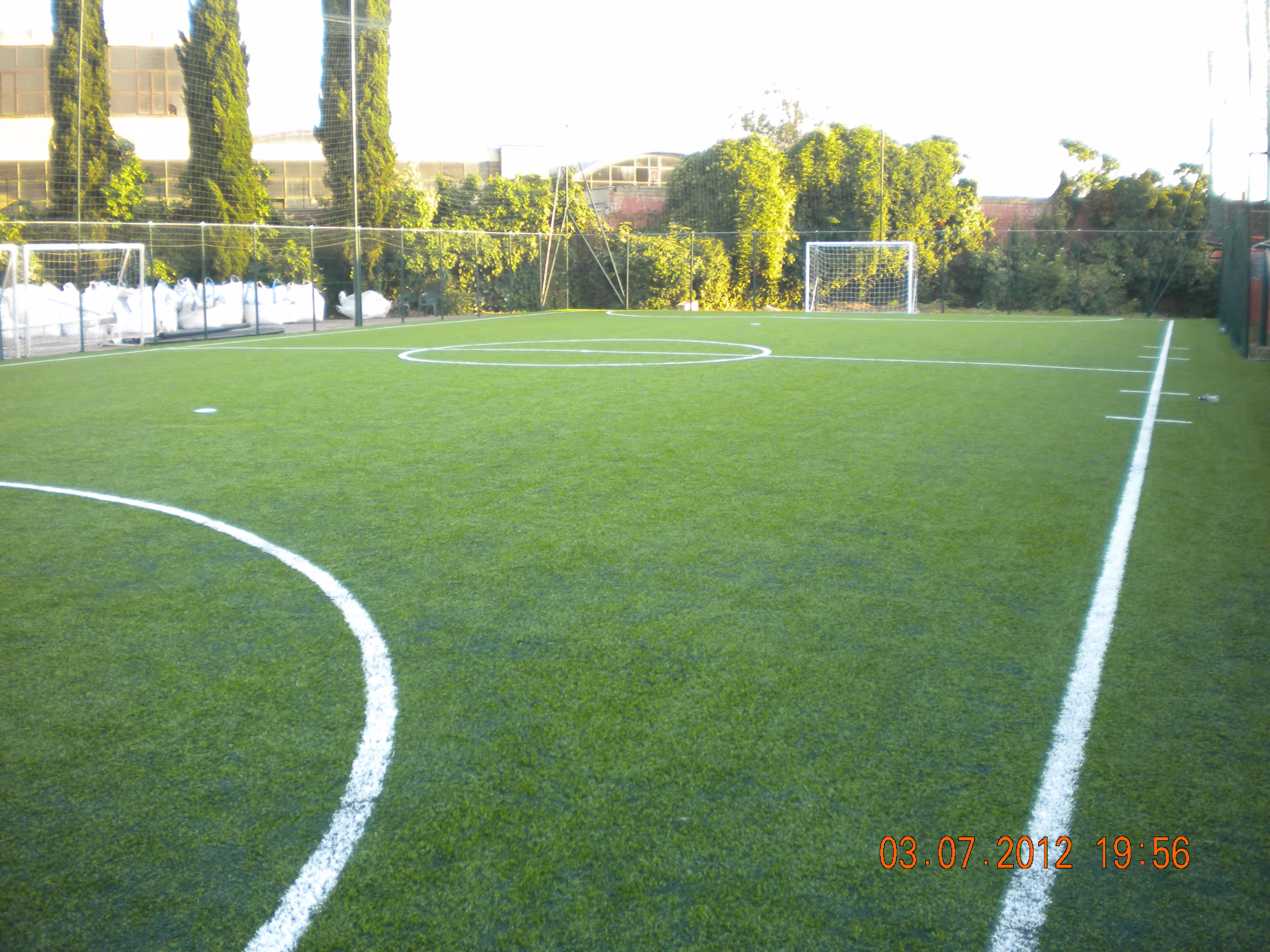 Campo di calcio a cinque con erba sintetica e due porte, circondato da alberi e cespugli.