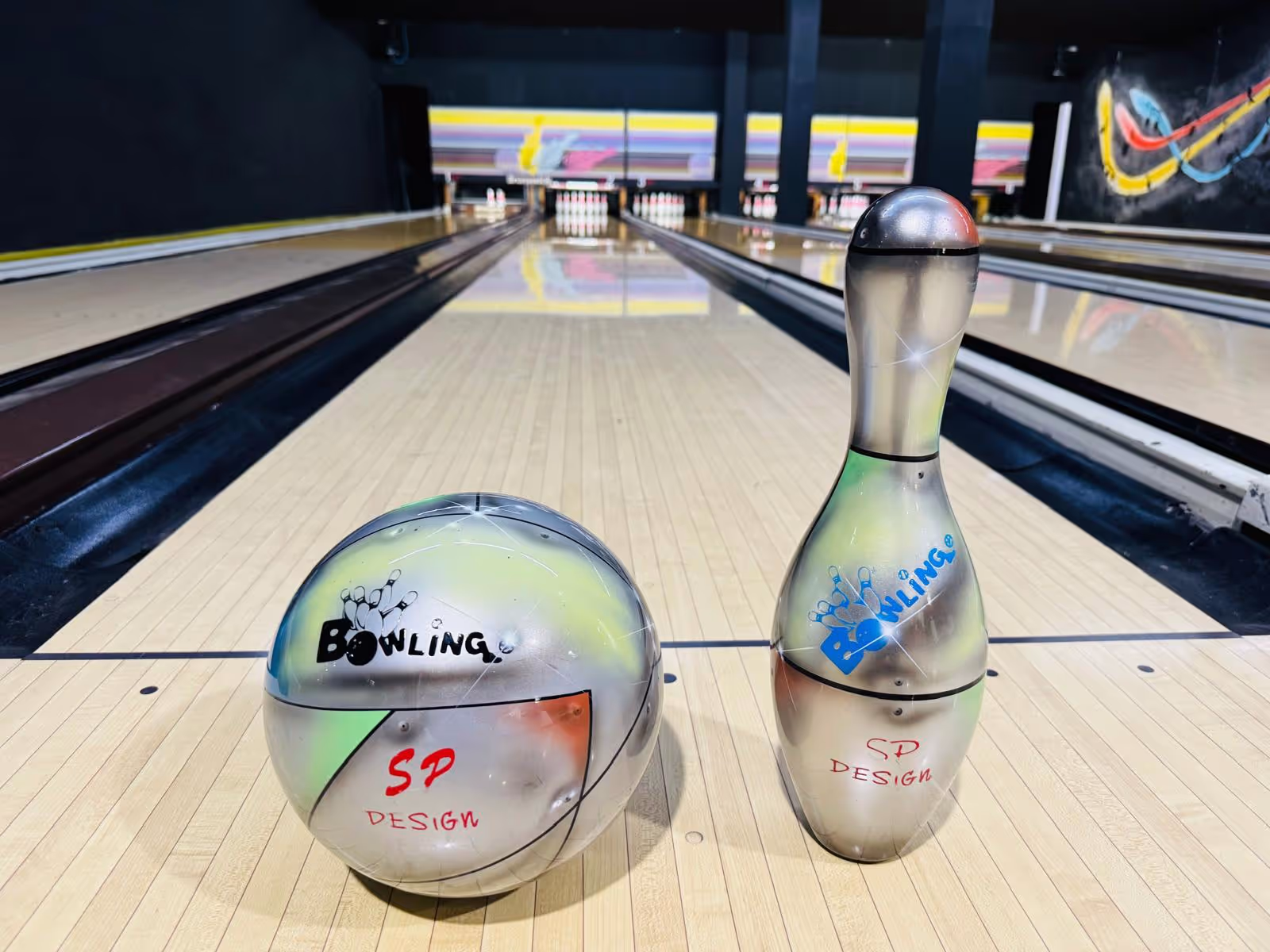 Palla e birillo da bowling con scritte 'Bowling' e 'SP Design' su una pista da bowling vuota.