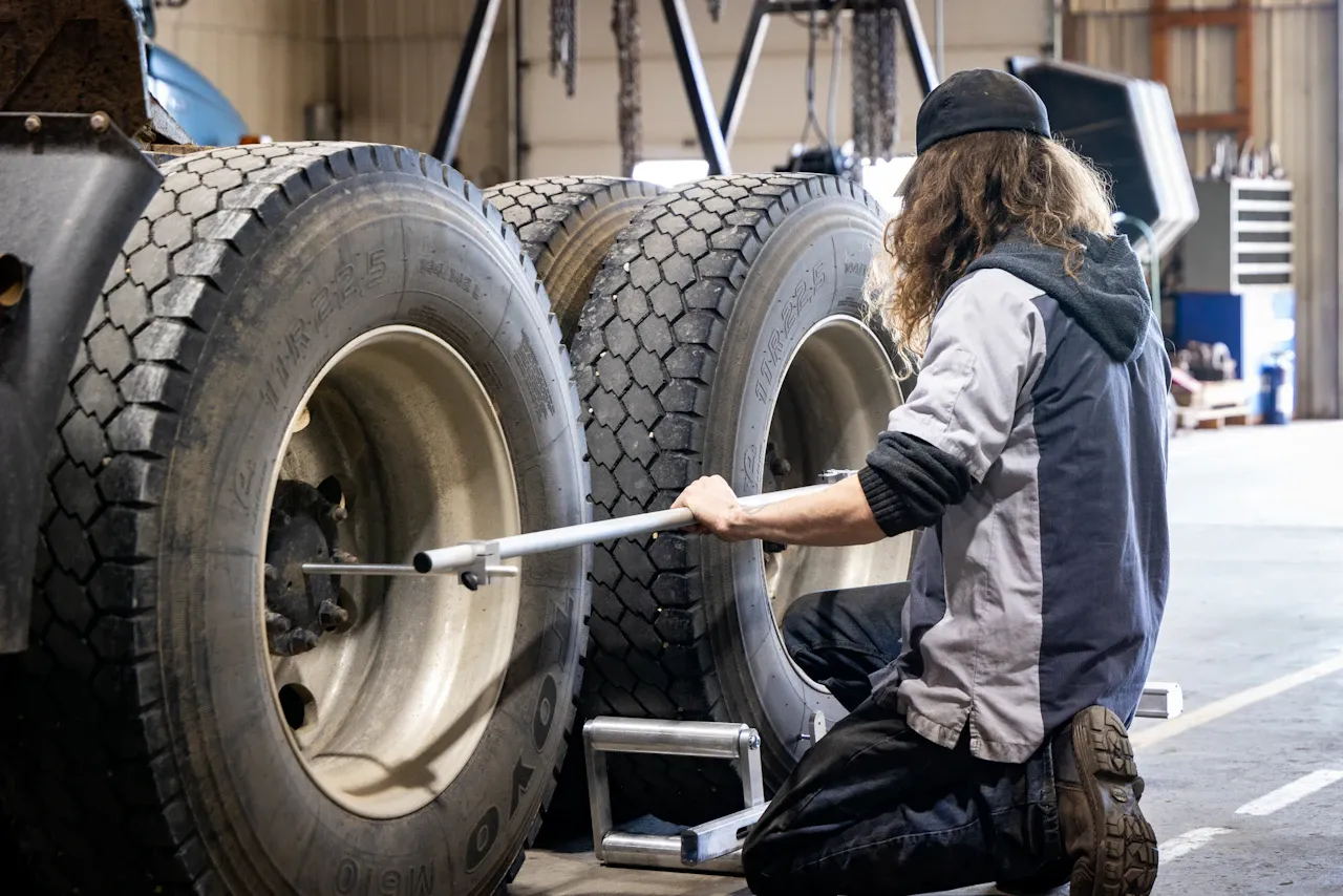 Tire service on a heavy-duty truck with technician performing wheel alignment in a commercial repair shop.