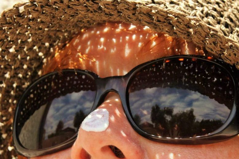 Close-up of a traveller in sunglasses and a straw hat with sun cream on their nose