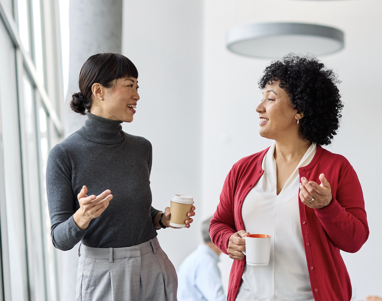 Two women chatting over coffee in a bright office