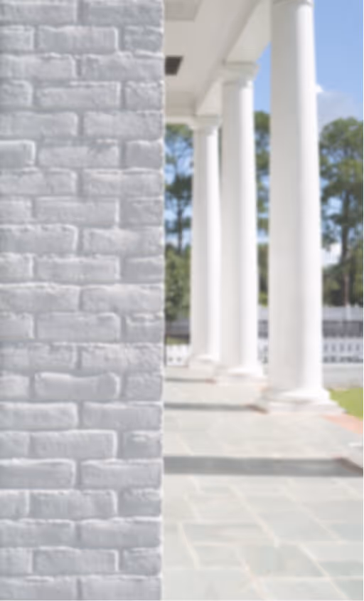 White brick wall on the left with a row of white columns along a stone-tiled walkway on the right.