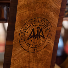 Close-up of a wooden surface with a circular engraving reading 'State of Louisiana, Union Justice Confidence' surrounding a pelican emblem.
