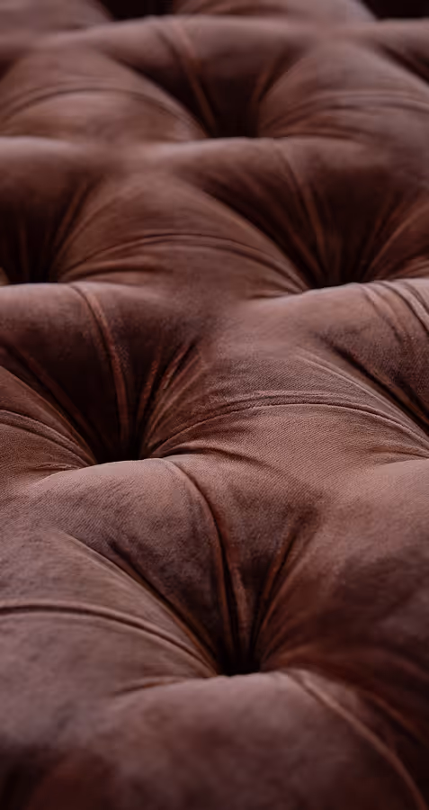 Close-up of brown tufted velvet upholstery with visible creases and buttoned indentations.